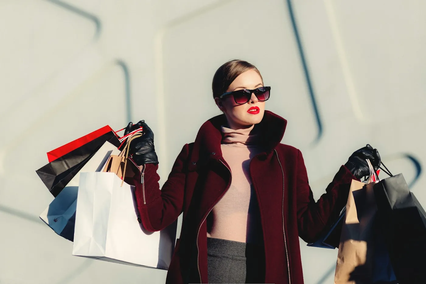 Woman wearing sunglasses and a burgundy coat holding shopping bags